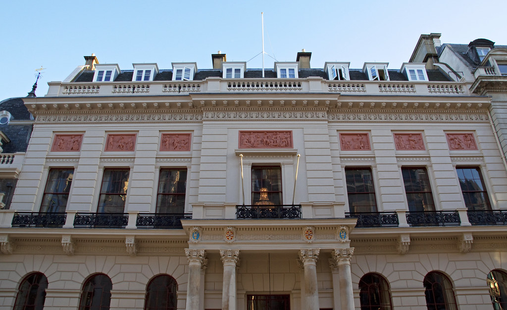 Front view of the Oxford and Cambridge Club, a historic building with a white stone façade, tall windows, decorative pink relief panels and a columned entrance.